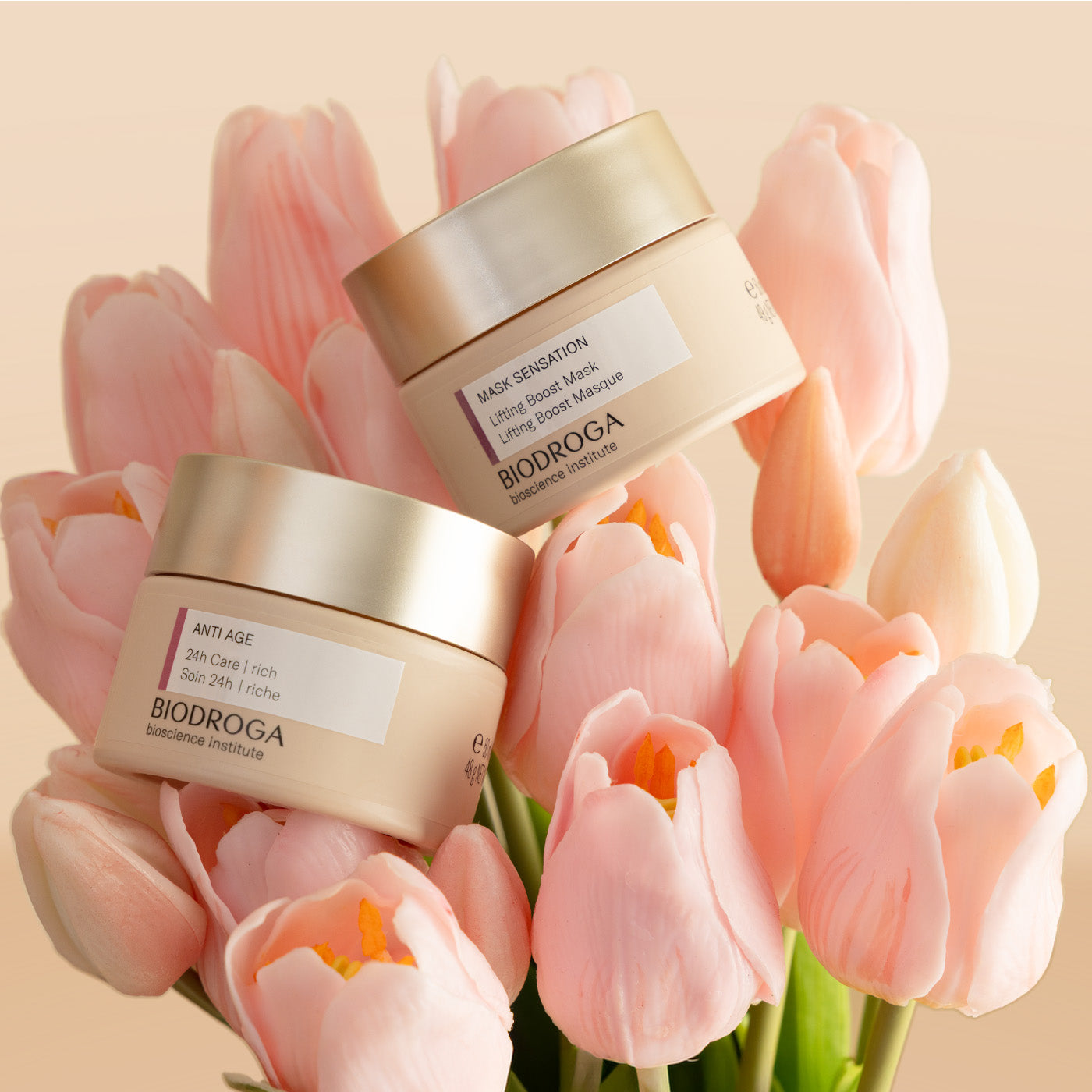 Two Biodroga skincare products surrounded by pink tulips on a soft peach background